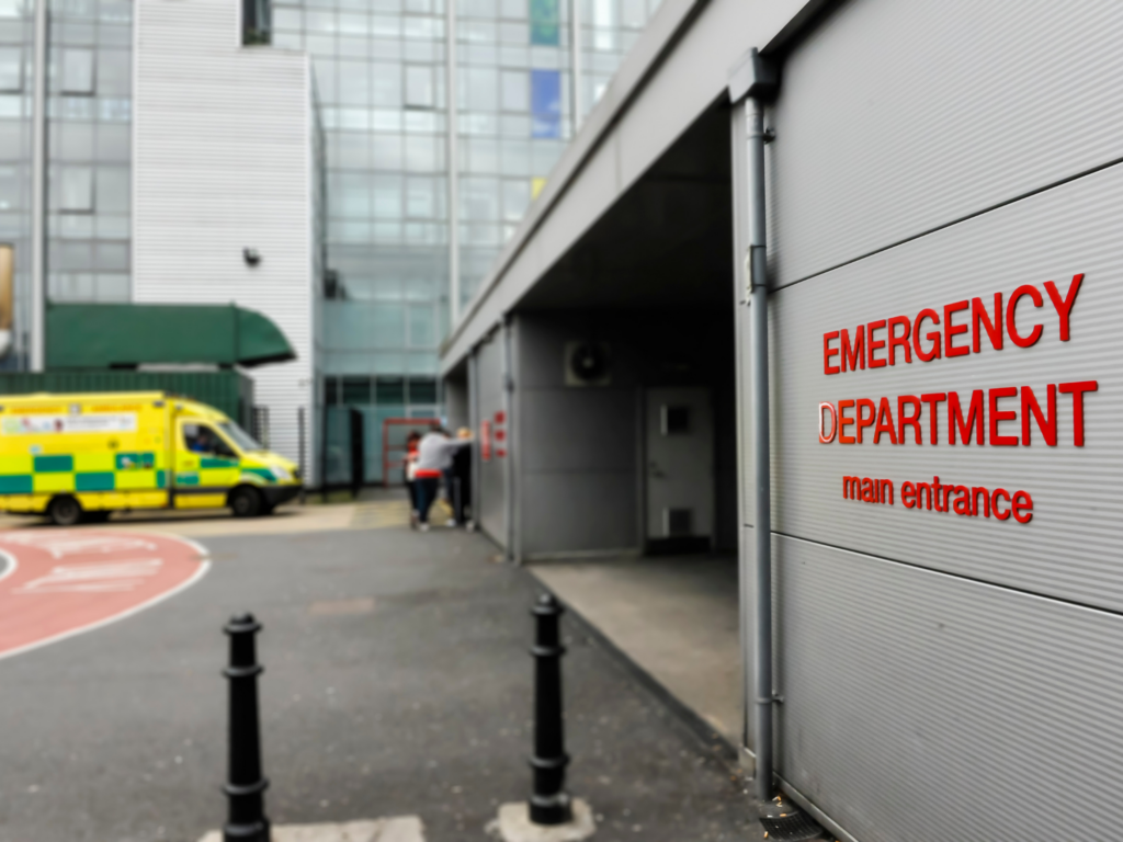 emergency department workforce review. Picture shows the outside of an emergency department, an ambulance can be seen in the distance.